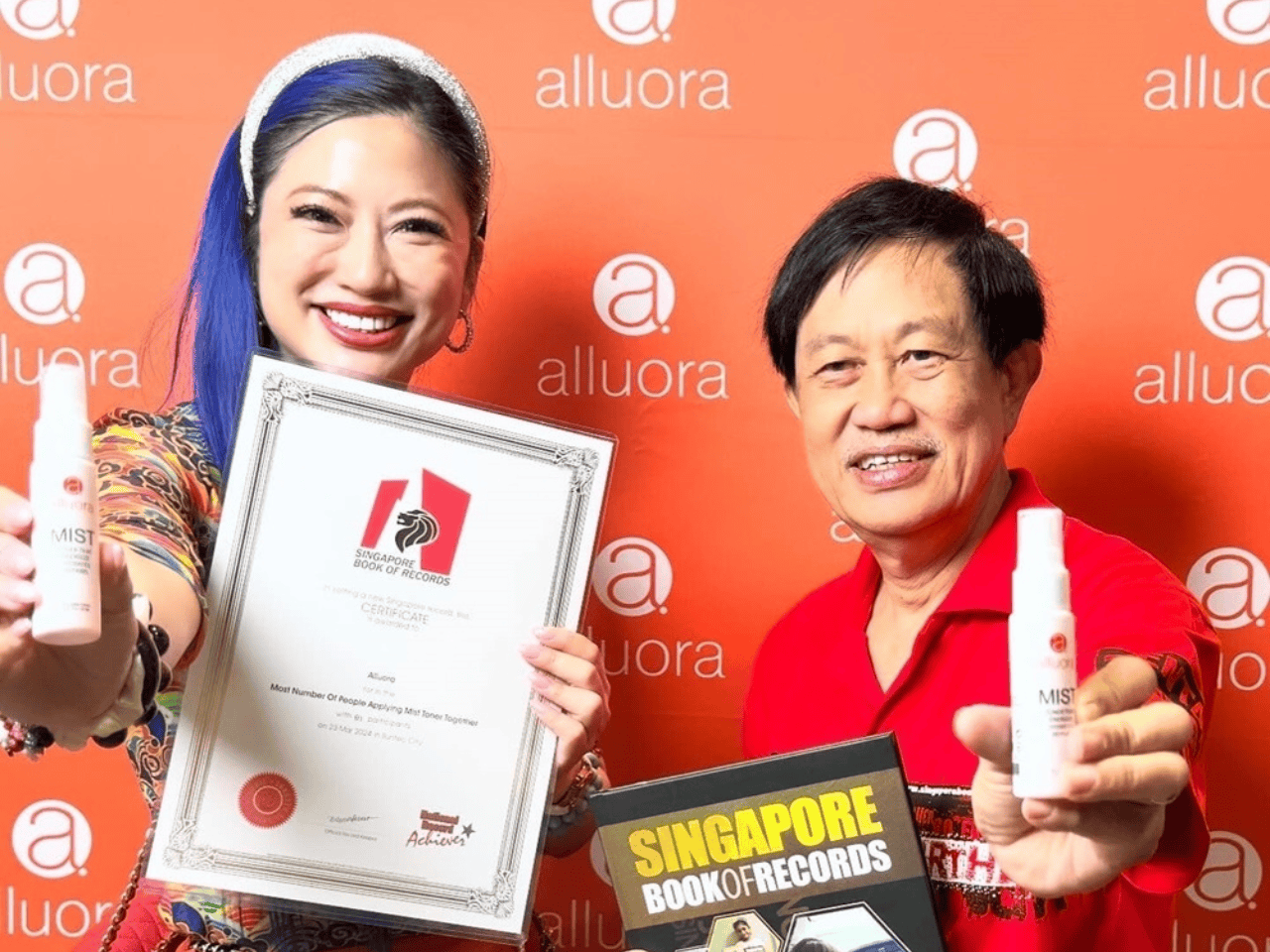 Elegant women and man showcasing skincare products and certificate at Alluora event in Singapore.