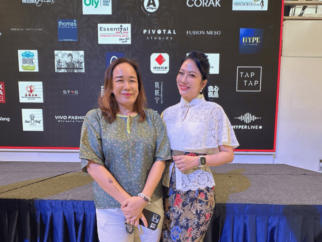 Alluora women at a fashion event, standing in front of a backdrop with brand logos, dressed in stylish, vibrant outfits.