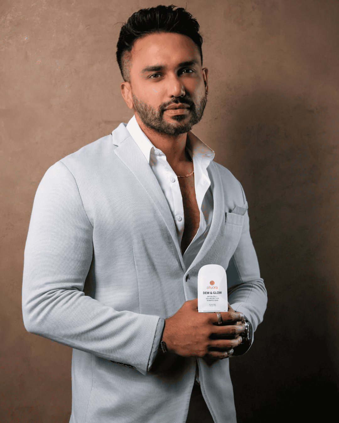 Bright-skinned man in a light gray suit holding Alluora sunscreen product, stylish and confident.